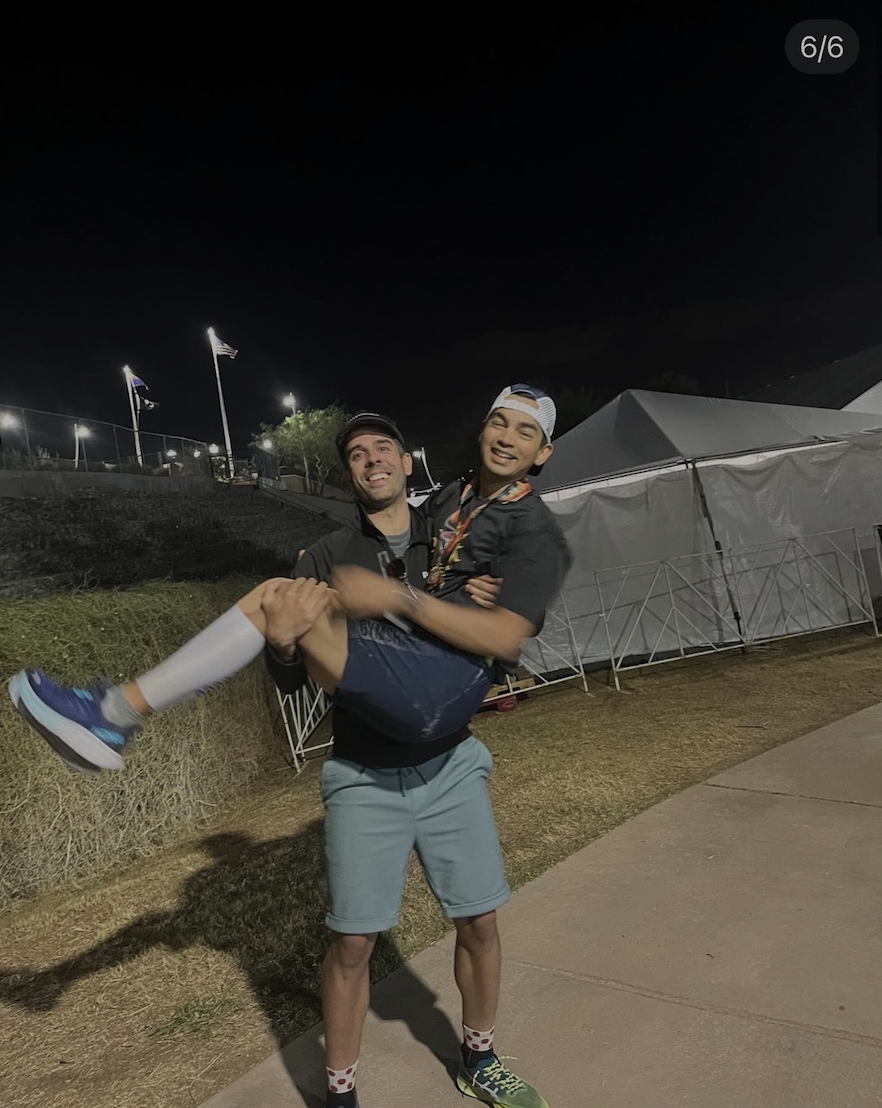 Breno Melo carrying a coached athlete across the IRONMAN Arizona finish chute after their first full-distance Ironman