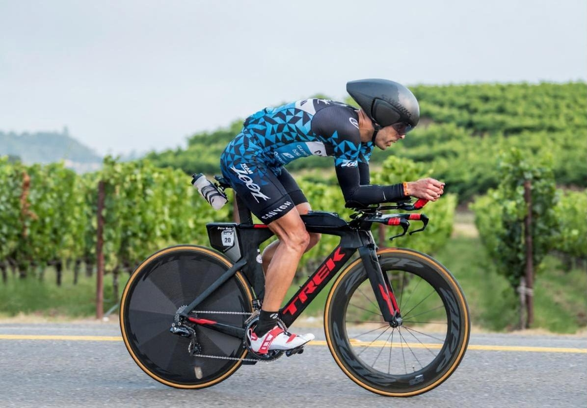 Breno Melo riding aero on a Trek time-trial bike past Napa vineyards during an IRONMAN 70.3 race