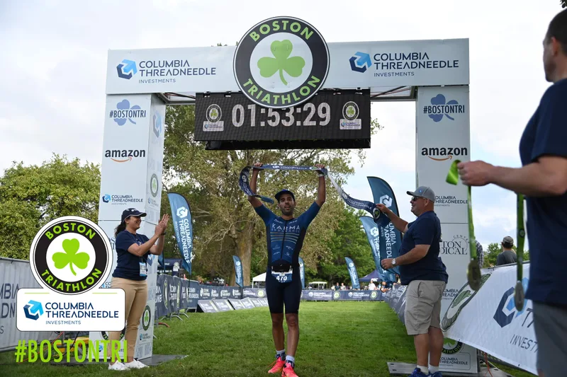 Breno crosses the Boston Triathlon finish line with arms raised