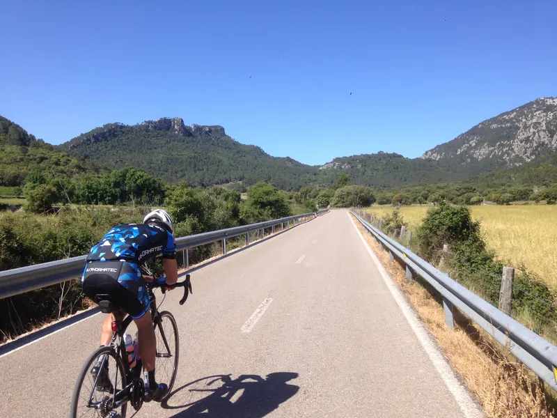 A cyclist in a blue kit rides along a road between mountains