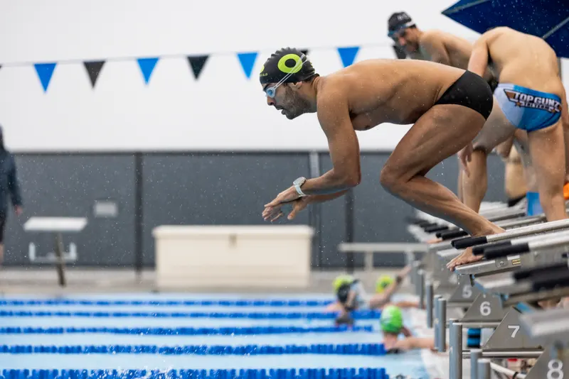 Swimmers lean forward on the starting blocks at an indoor pool